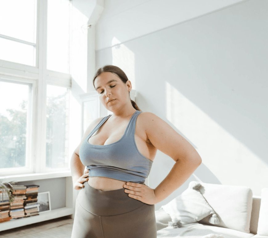 Young woman standing in a bright room with hands on hips, reflecting on her weight loss journey and considering gastric sleeve surgery.